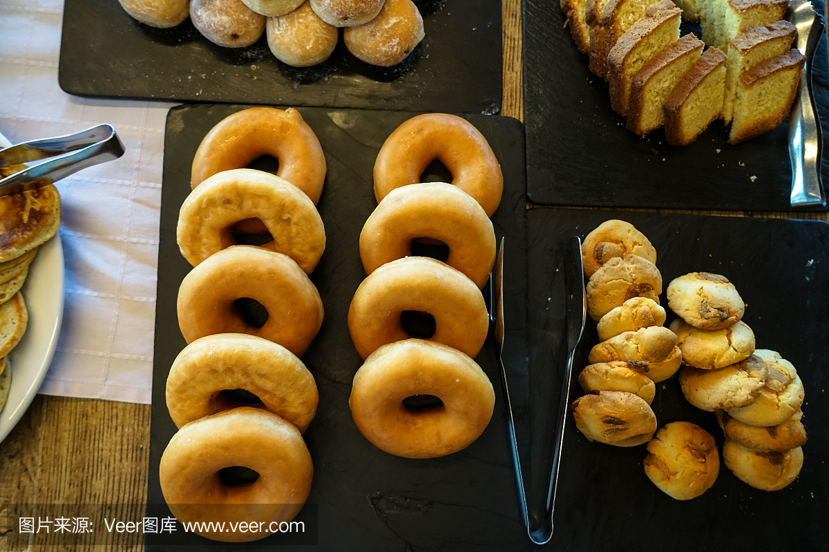 希臘自助早餐桌上有一盤盤的甜烘焙甜點(diǎn),包括甜甜圈、餅干、奶油蛋糕、小面包等